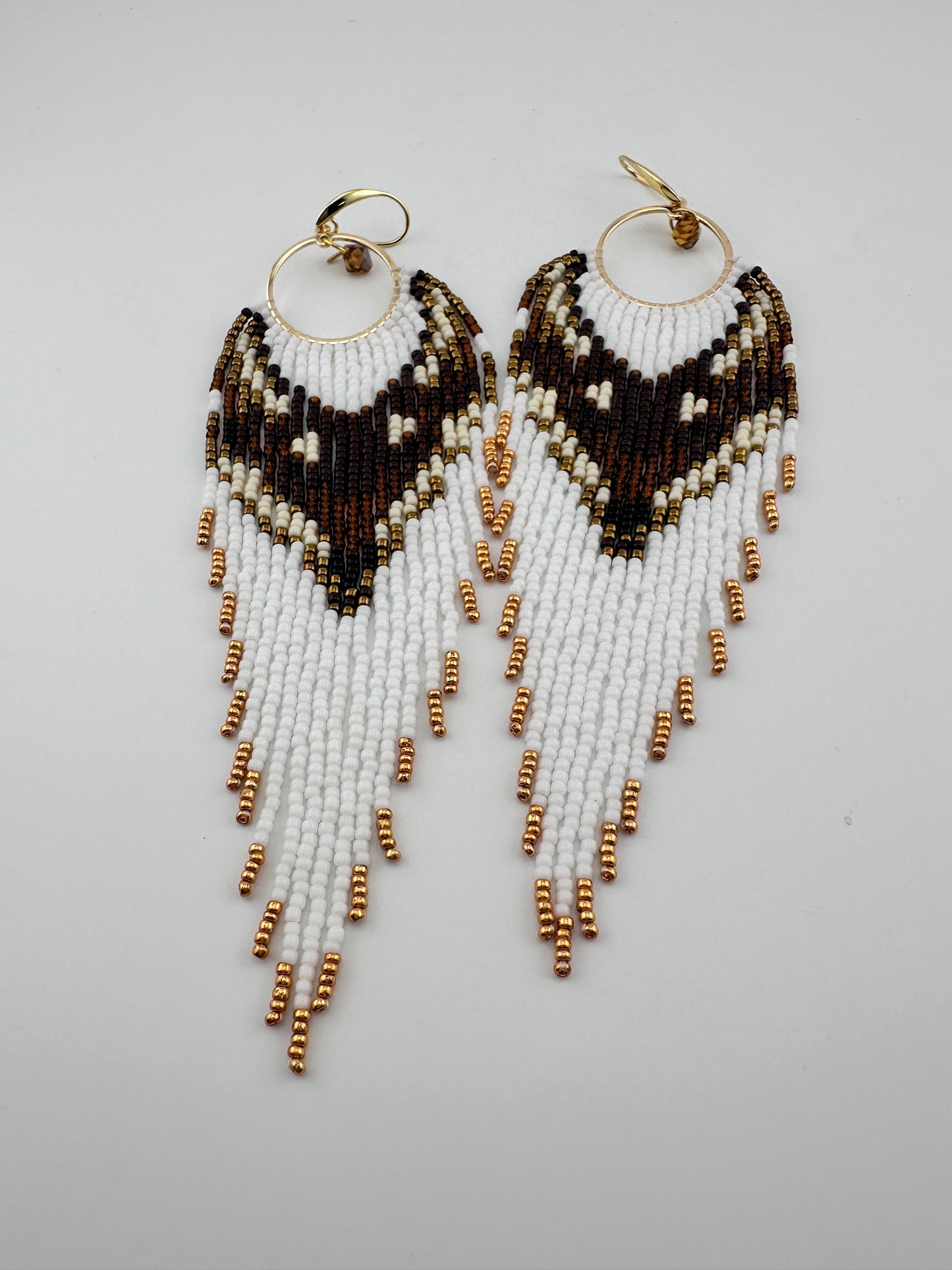Handmade beaded hoop earrings with gold hooks, featuring white, brown, black, and gold seed beads in a chevron fringe pattern, displayed on a white background.