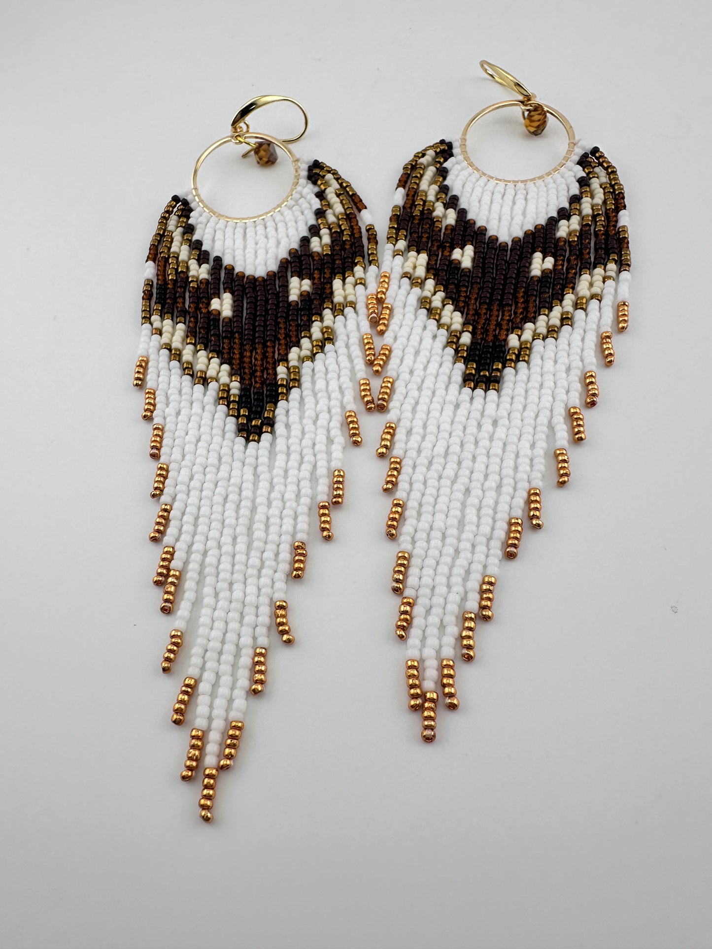 
Handmade beaded hoop earrings with gold hooks, featuring white, brown, black, and gold seed beads in a chevron fringe pattern, displayed on a white background.