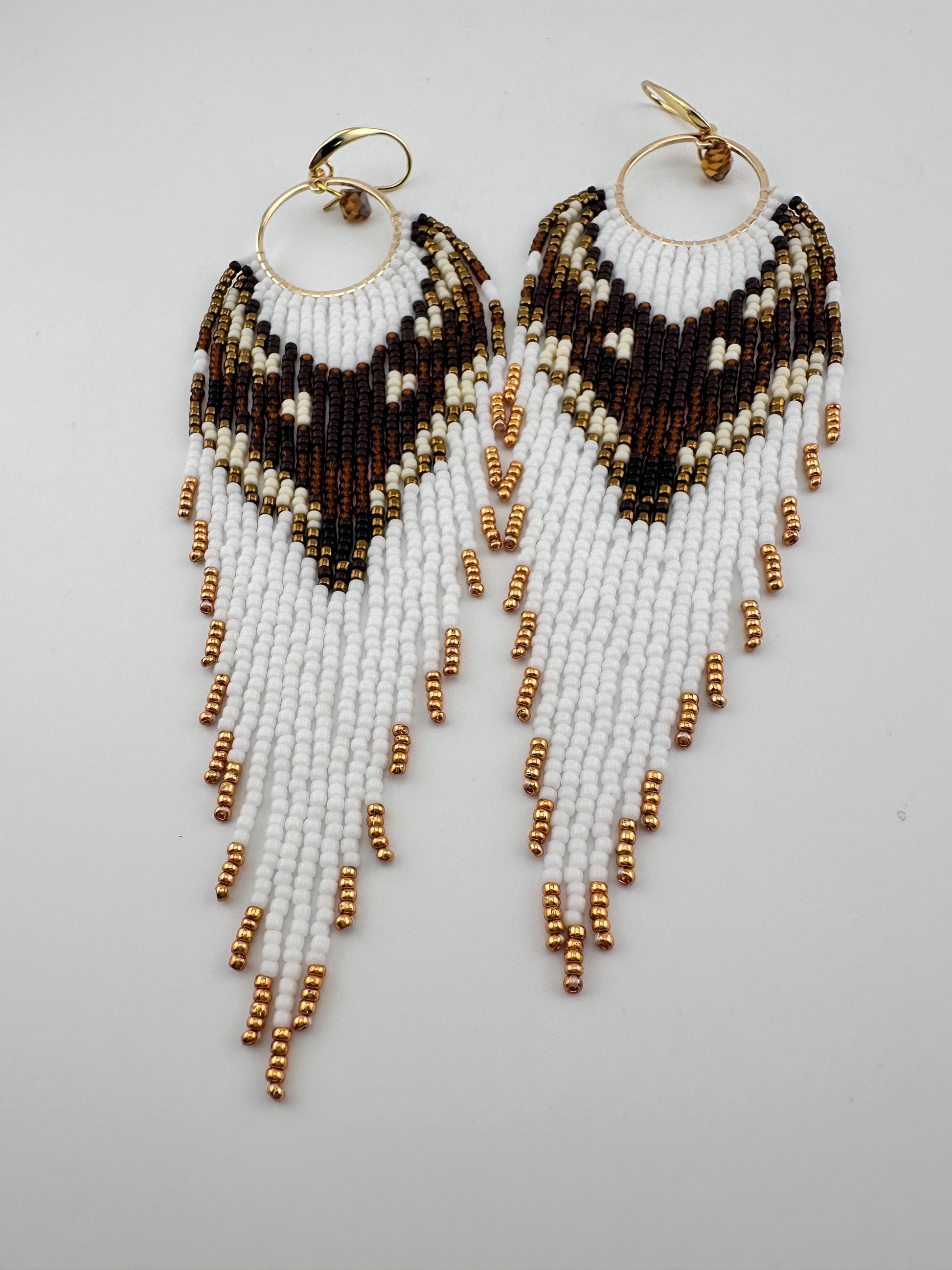 
Handmade beaded hoop earrings with gold hooks, featuring white, brown, black, and gold seed beads in a chevron fringe pattern, displayed on a white background.