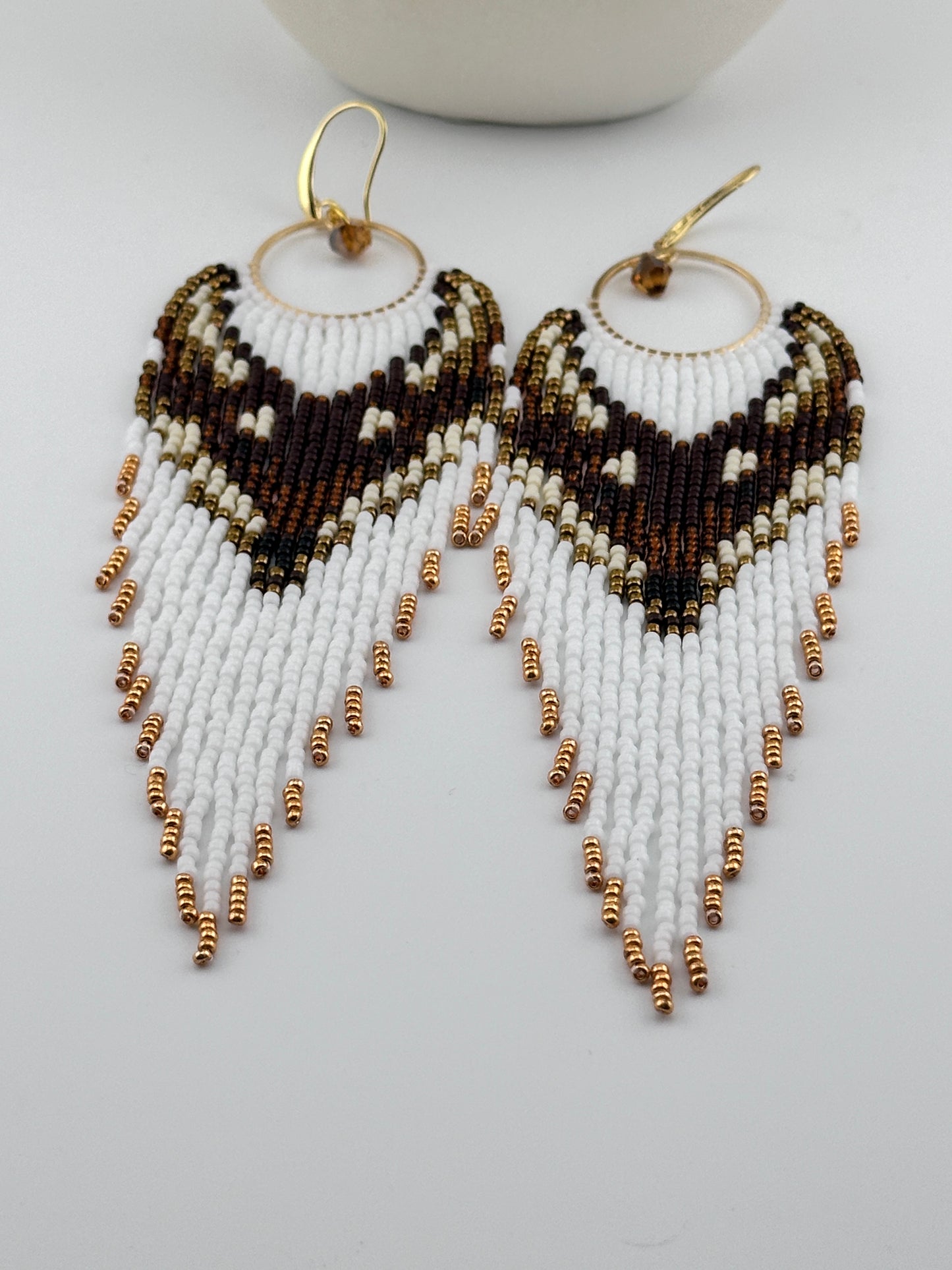 
Handmade beaded hoop earrings with gold hooks, featuring white, brown, black, and gold seed beads in a chevron fringe pattern, displayed on a white background.