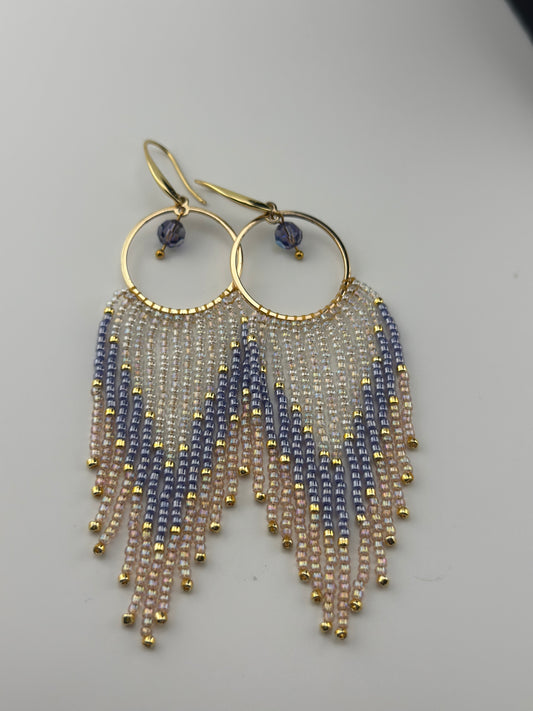 Handmade gold hoop earrings with soft pink, lavender, and pearl white seed bead fringe in a chevron pattern, finished with gold accents and purple crystal dangles