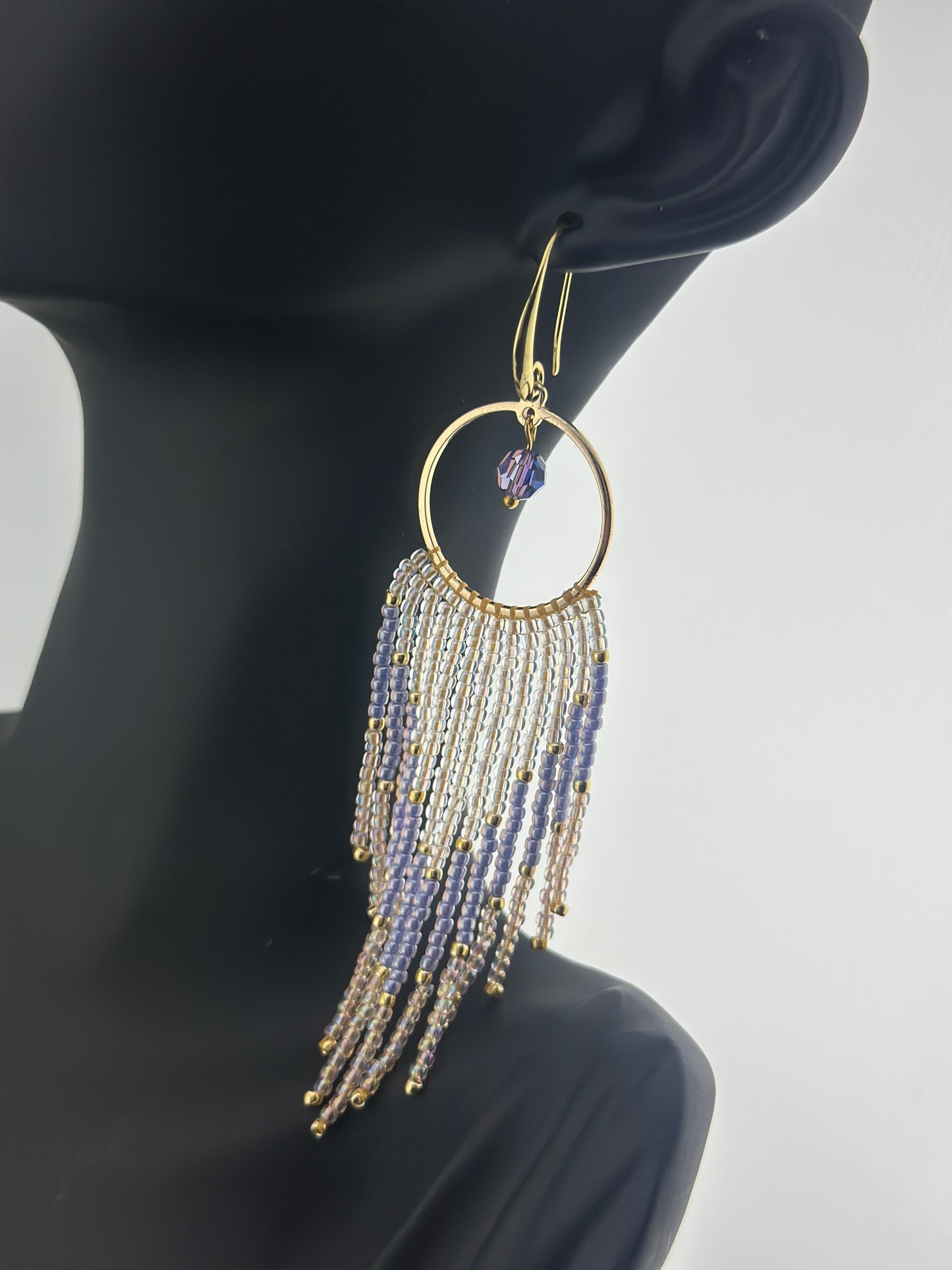 Handmade gold hoop earrings with soft pink, lavender, and pearl white seed bead fringe in a chevron pattern, finished with gold accents and purple crystal dangles