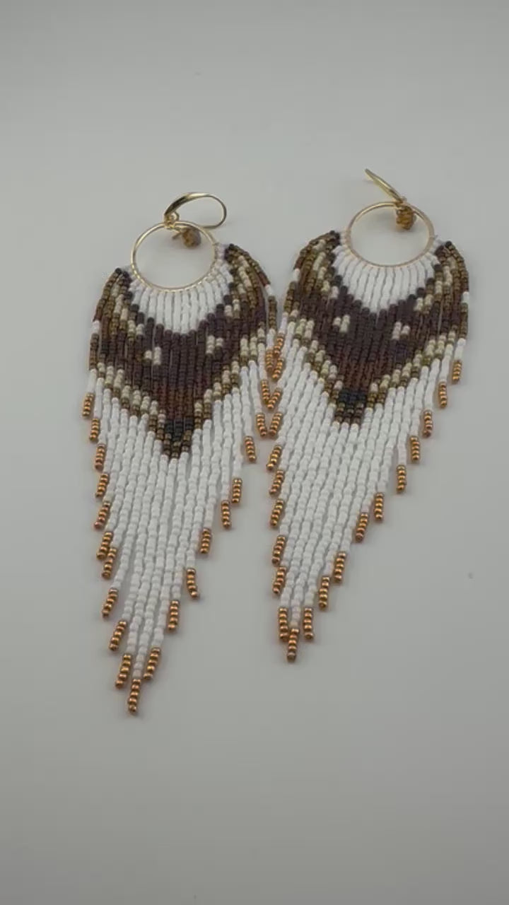 
Handmade beaded hoop earrings with gold hooks, featuring white, brown, black, and gold seed beads in a chevron fringe pattern, displayed on a white background.